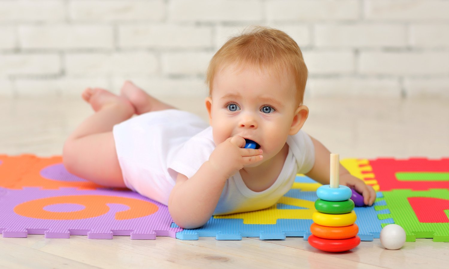 Ein bäuchlings liegendes Baby nimmt buntes Plastikspielzeug in den Mund