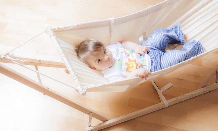 Ein Kleinkind liegt in einem Zimmer in einer hellen Hängematte