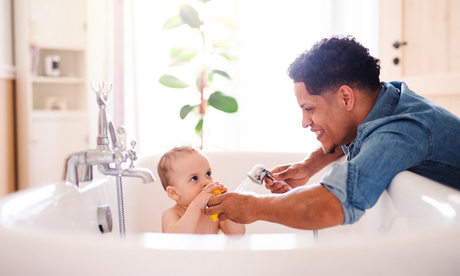 Ein Mann badet ein Baby in der Badewanne im lichtdurchfluteten Badezimmer