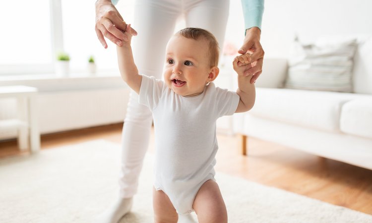 Baby lernt an den Händen seiner Mutter laufen