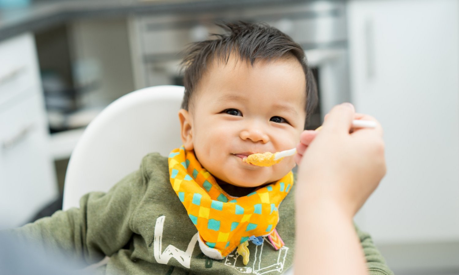 Ein Kleinkind wird mit einem Löffel Brei im Hochstuhl gefüttert