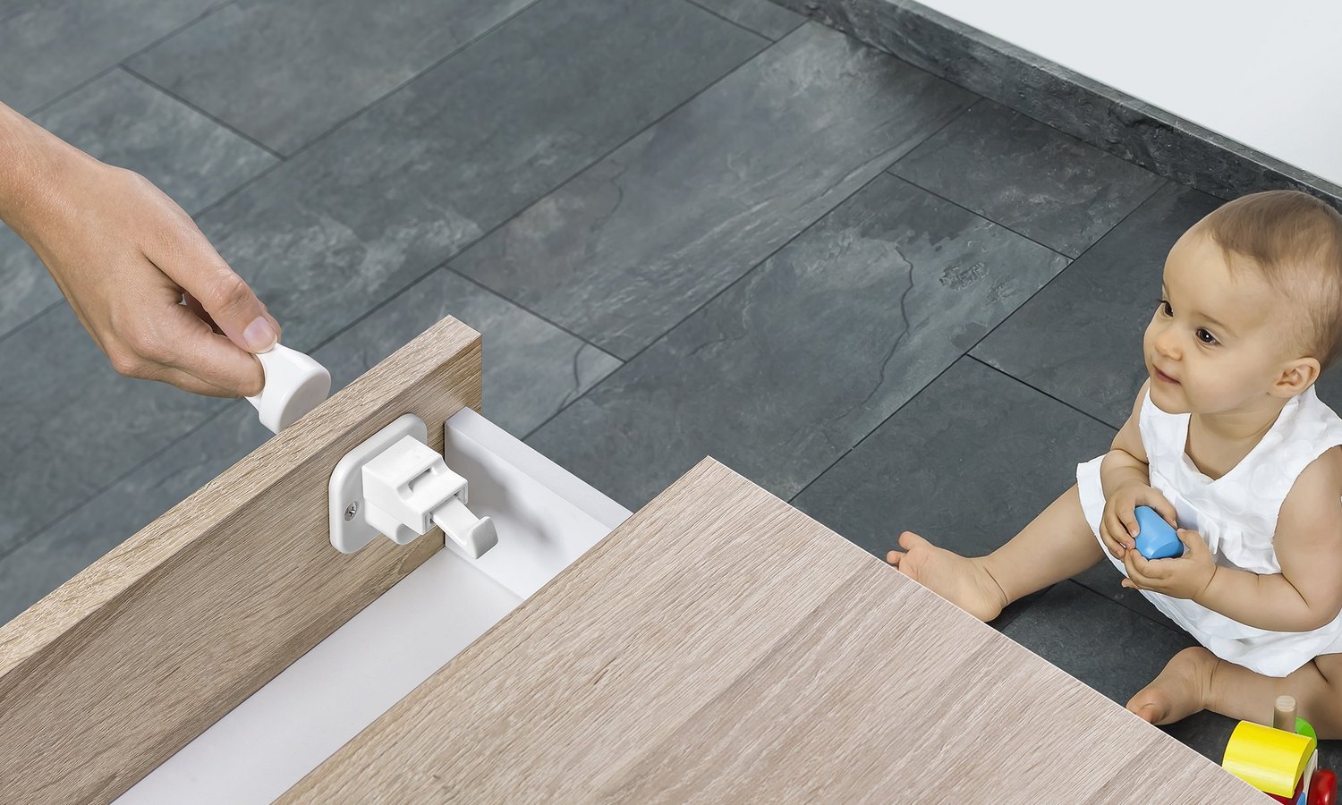 Eine Hand öffnet eine magnetisch gesicherte Schublade unter den Augen eines Babys