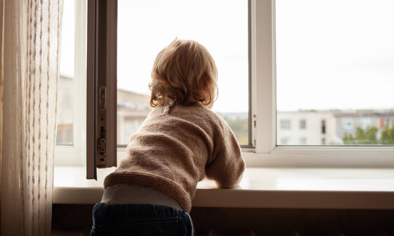 Ein Kleinkind lehnt auf der Fensterbank am geöffneten Fenster