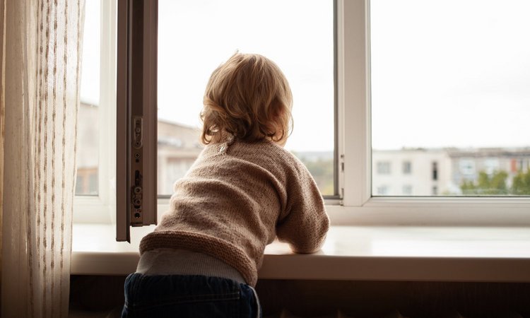 Ein Kleinkind lehnt auf der Fensterbank am geöffneten Fenster
