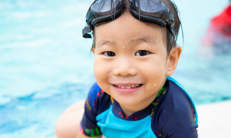 Ein Junge mit Taucherbrille Sitz lächelnd am Beckenrand eines Schwimmbeckens