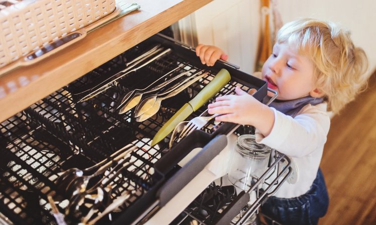 Ein Kleinkind greift in die Besteckablage der geöffneten Spülmaschine