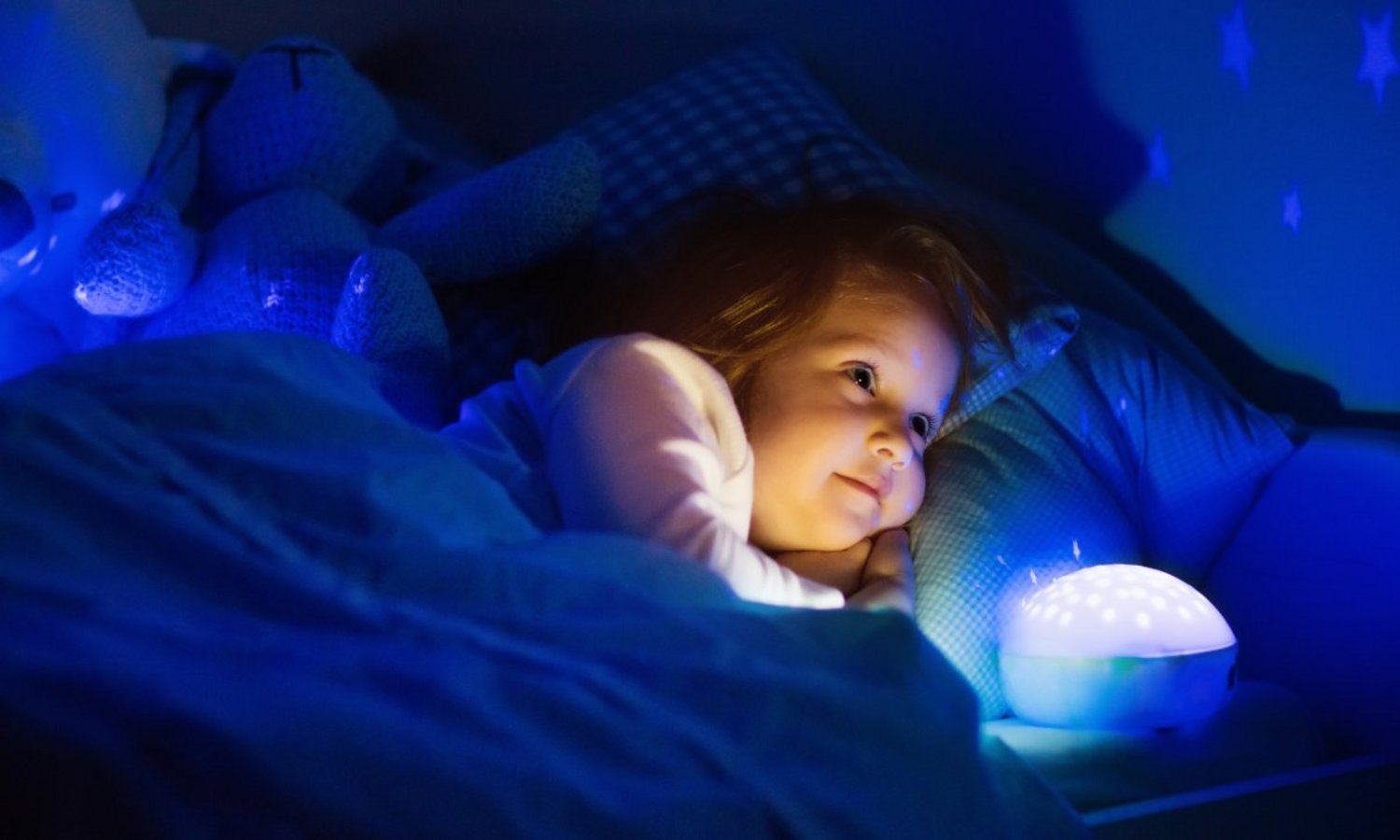 Ein Kind liegt im dunklen Zimmer im Bett neben einem hell leuchtenden Nachtlicht