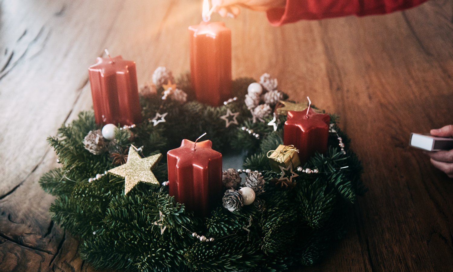 Eine Hand zündet mit Streichhölzern die erste Kerze am Adventskranz an